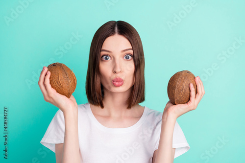 Photo of funny brunette hair young lady hold coconuts blow kiss wear white t-shirt isolated on teal color background