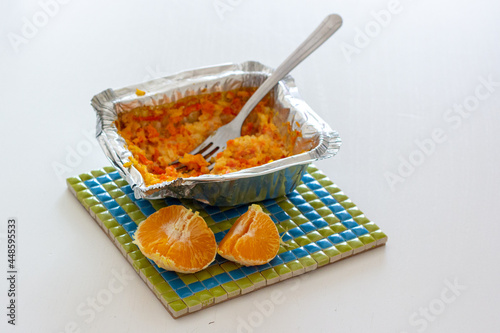 Carrot rice porridge in foil packaging and half of tangerine on a heat trivet.
