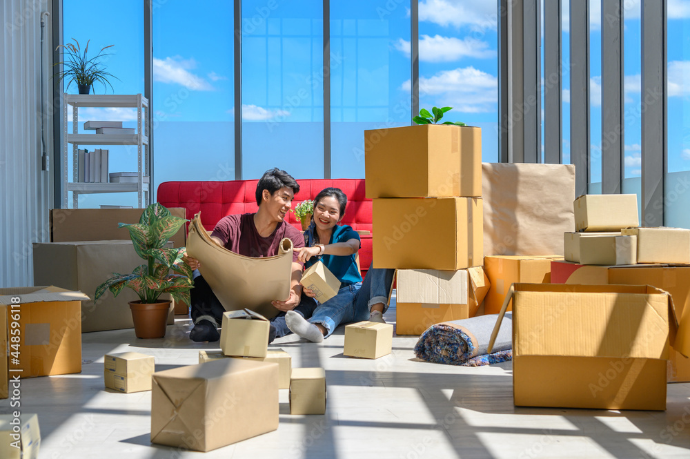 Fototapeta premium Young asian couple smiling, relaxing and resting on the floor after unpacking cardboard boxes in new house with cardboard boxes on floor
