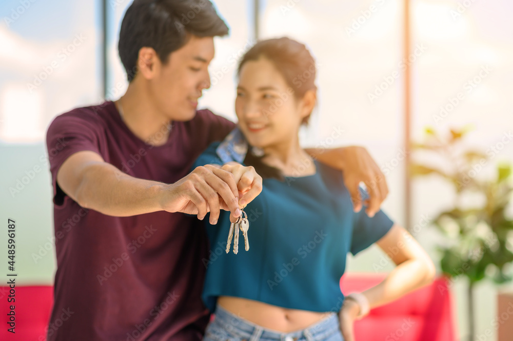 Naklejka premium Happy young asian married couple holding key while relocation into new home on moving day, celebrating moving to new home concept