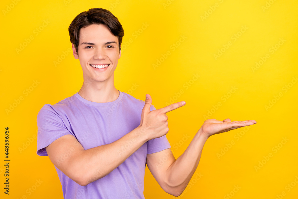 Portrait of attractive cheerful guy demonstrating holding on palm offer copy space ad isolated over bright yellow color background