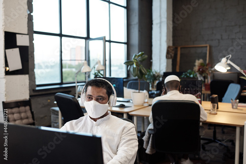 Young contemporary office manager in protective mask working in the net in front of computer