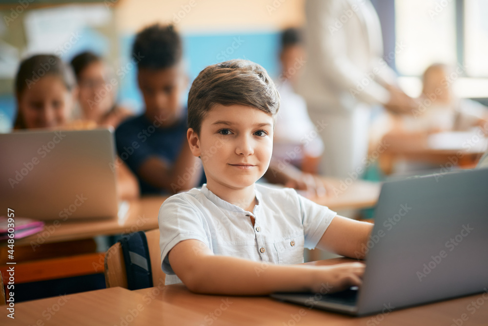 Fototapeta premium Elementary student using laptop on class at school and looking at camera.