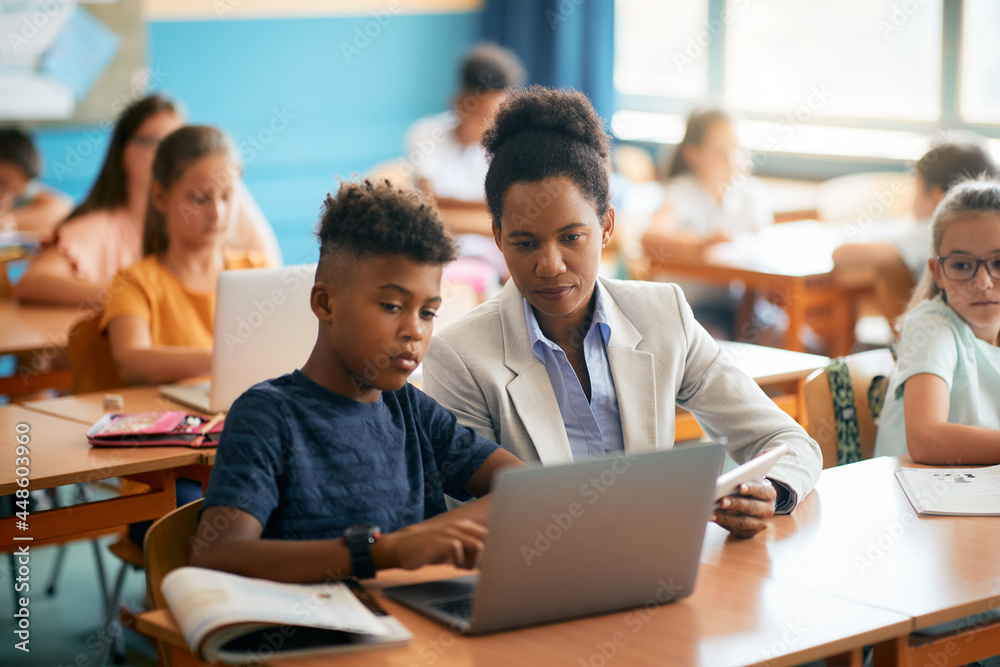 African American teacher and her student using laptop during computer class at elementary school. African American teacher and her student using laptop during computer class at elementary school.