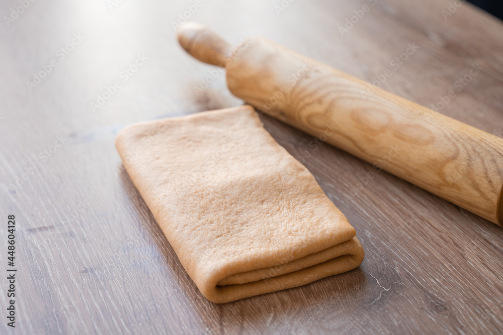 Side view of folded croissant dough, laminated dough and rolling pin on wooden table. lamination. Side view of folded croissant dough, laminated dough and rolling pin on wooden table. lamination.