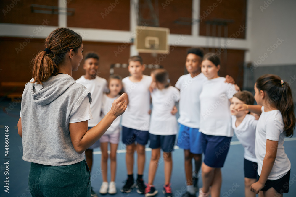 Obraz premium Rear view of physical education teacher talking to her students on class at school gym.
