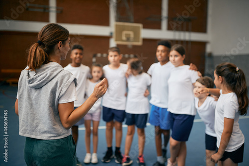 Rear view of physical education teacher talking to her students on class at school gym.