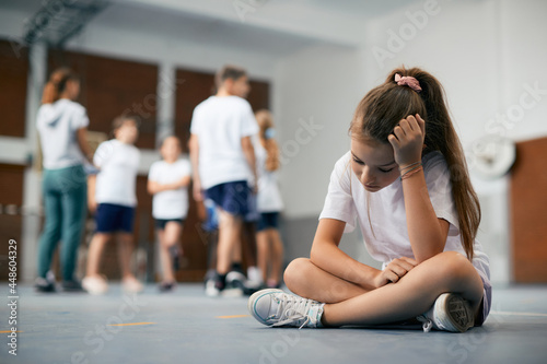 Sad schoolgirl feeling left out during physical activity class at school gym.