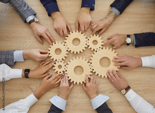 Team of business people join gearwheels. High angle, overhead view of circle of hands holding cogs on office table. Metaphor for good effective business system, cooperation, teamwork and efficiency photo