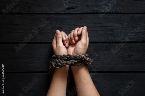 Photography tied female hands with an old rope on a black wooden board background, tied hand