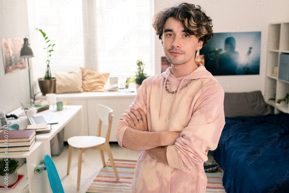 Cross-armed teenager in pink hoodie looking at camera in his bedroom Cross-armed teenager in pink hoodie looking at camera in his bedroom