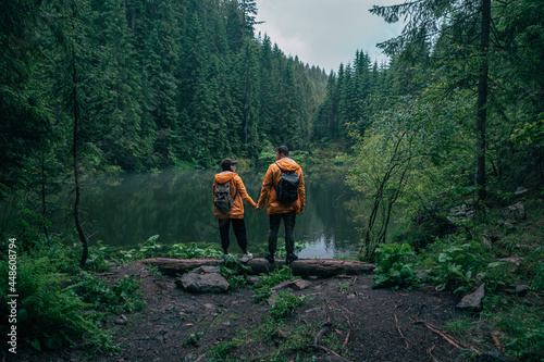 couple hikers in yellow raincoat looking at mountain lake