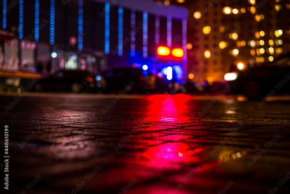 Rainy night in the big city, light from the shop windows and the windows of the house is reflected in the asphalt. View from the sidewalk level paved with bricks Rainy night in the big city, light from the shop windows and the windows of the house is reflected in the asphalt. View from the sidewalk level paved with bricks
