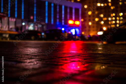 Rainy night in the big city, light from the shop windows and the windows of the house is reflected in the asphalt. View from the sidewalk level paved with bricks