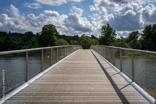 Canvas Print Perspective summer view of a wooden pedestrian bridge with water, cloudy sky and horizon in the background