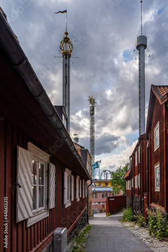 Photography Perspective view of old vintage red wooden buildings in Stockholm with the amusement park towers of Gröna Lund in the background