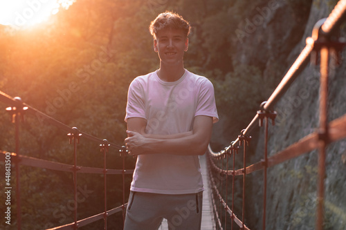 Hombre joven de brazos cruzados con felicidad haciendo senderismo con vegetación y puesta de sol en un punte junto a las montañas y naturaleza photo
