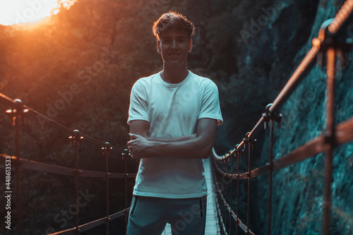 Hombre joven de brazos cruzados con felicidad haciendo senderismo con vegetación y puesta de sol en un punte junto a las montañas y naturaleza photo
