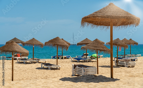 View of the luxury beach on sea with sun loungers and umbrellas, in tourist zone of tropics. Sunny day and In the background is a sailboat yacht. © sergojpg