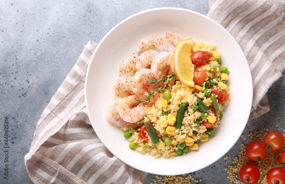 Seafood dish. Shrimp with couscous and vegetables: asparagus beans, corn, tomatoes, green peas and lemon in a white plate on grey table. Background image, copy space Seafood dish. Shrimp with couscous and vegetables: asparagus beans, corn, tomatoes, green peas and lemon in a white plate on grey table. Background image, copy space
