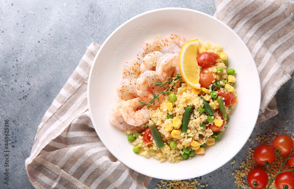 Seafood dish. Shrimp with couscous and vegetables: asparagus beans, corn, tomatoes, green peas and lemon in a white plate on grey table. Background image, copy space