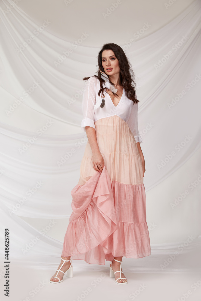 Beautiful sexy woman wear light pink multicolor dress summer collection silk casual style tanned body brunette hair beautiful face makeup white background studio. Beautiful sexy woman wear light pink multicolor dress summer collection silk casual style tanned body brunette hair beautiful face makeup white background studio.