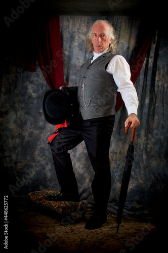 A well-dressed victorian steampunk, holding top hat and coat and leaning on the umbrella, wearing double-breasted trousers, gray vest with a pocket watch.