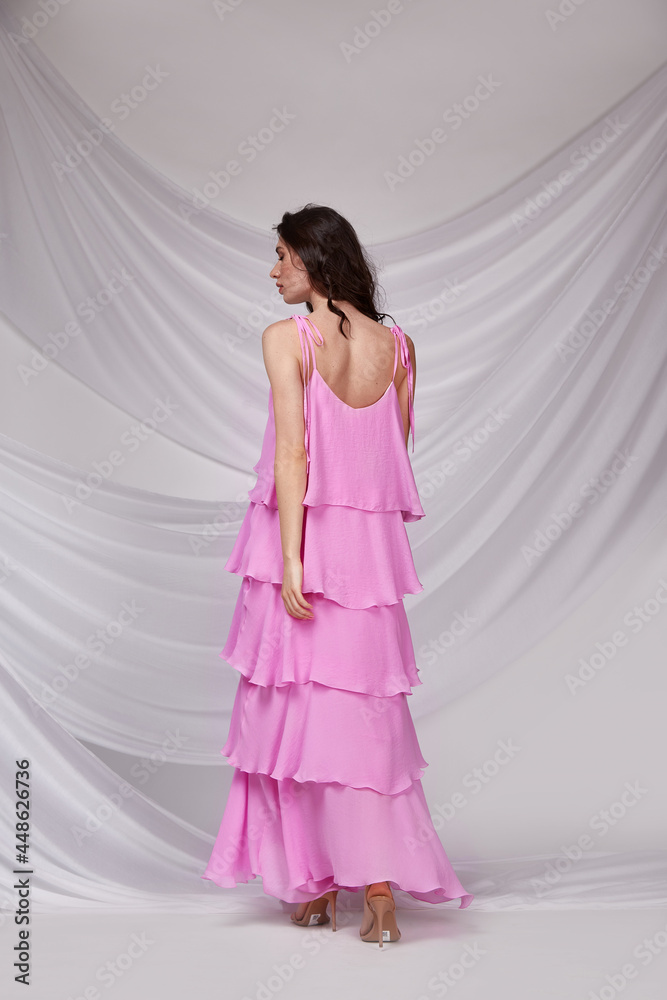 Beautiful sexy woman wear light long pink color dress summer collection cotton casual style tanned body brunette hair beautiful face makeup white background studio.