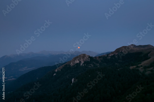 Full red moon. Splendid full red moon rises over the mountain ridges of the Apennines.