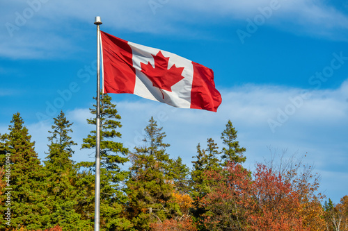 Canadian flag flying in a brisk wind over an autumn landscape.