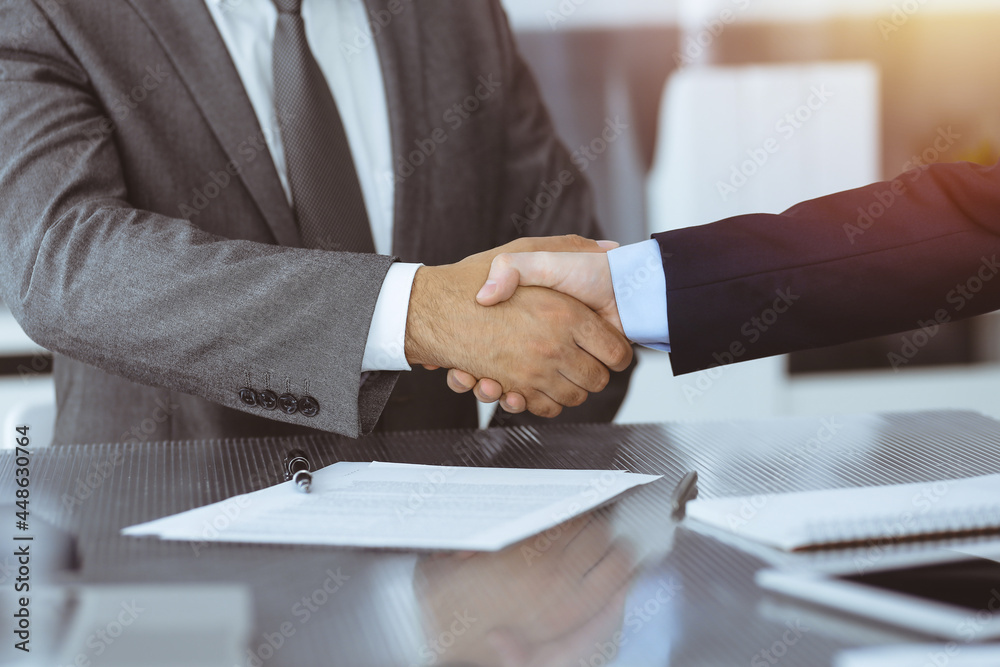 Unknown business people are shaking hands after contract signing in modern office, close-up. Handshake as successful negotiation ending