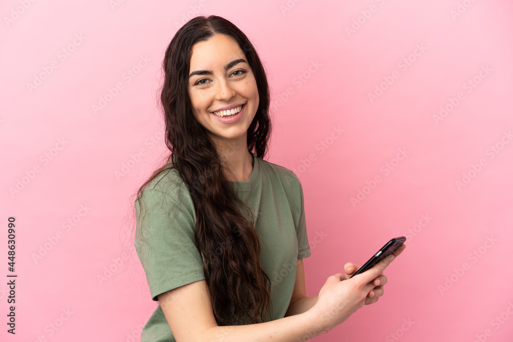 Young caucasian woman isolated on pink background sending a message or email with the mobile Young caucasian woman isolated on pink background sending a message or email with the mobile