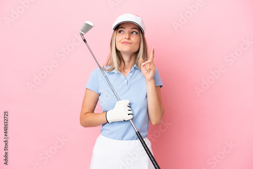 Young golfer player woman isolated on pink background with fingers crossing and wishing the best
