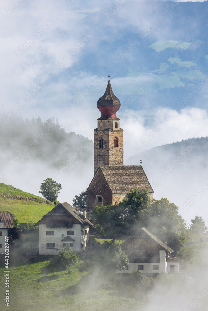 Small photogenic stone catholic church in Italian village with dramatic fog