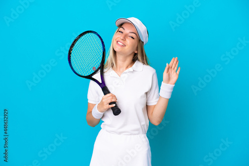 Young tennis player Romanian woman isolated on blue background saluting with hand with happy expression © luismolinero