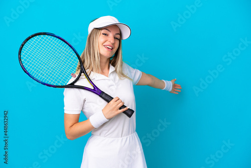 Young tennis player Romanian woman isolated on blue background extending hands to the side for inviting to come © luismolinero