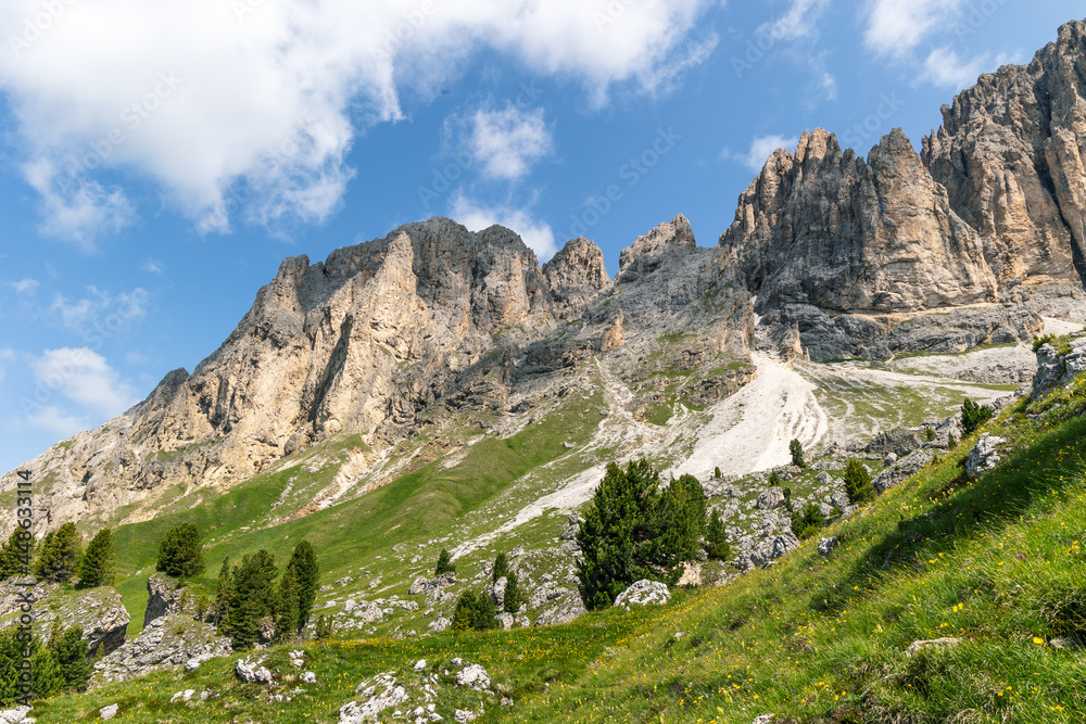 Dramatic rocky mountain peaks rising out of the green hills in the Dolomite mountains