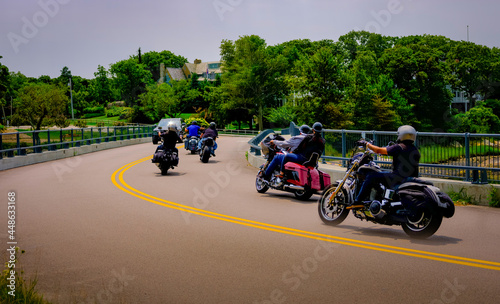 Group of bikers riding over the curved bridge on a sunny foggy day.