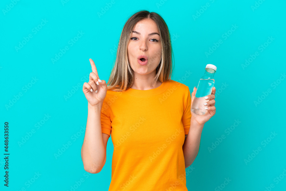 Young Romanian woman with a bottle of water isolated on blue background intending to realizes the solution while lifting a finger up Young Romanian woman with a bottle of water isolated on blue background intending to realizes the solution while lifting a finger up
