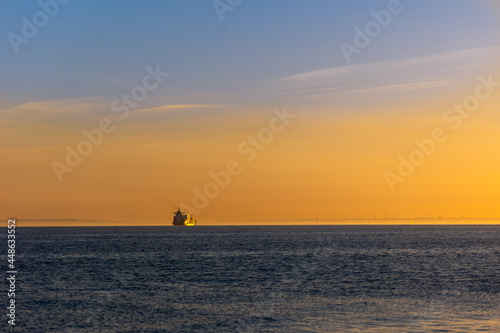 Small container ship sailing towards the horizon on a calm ocean 