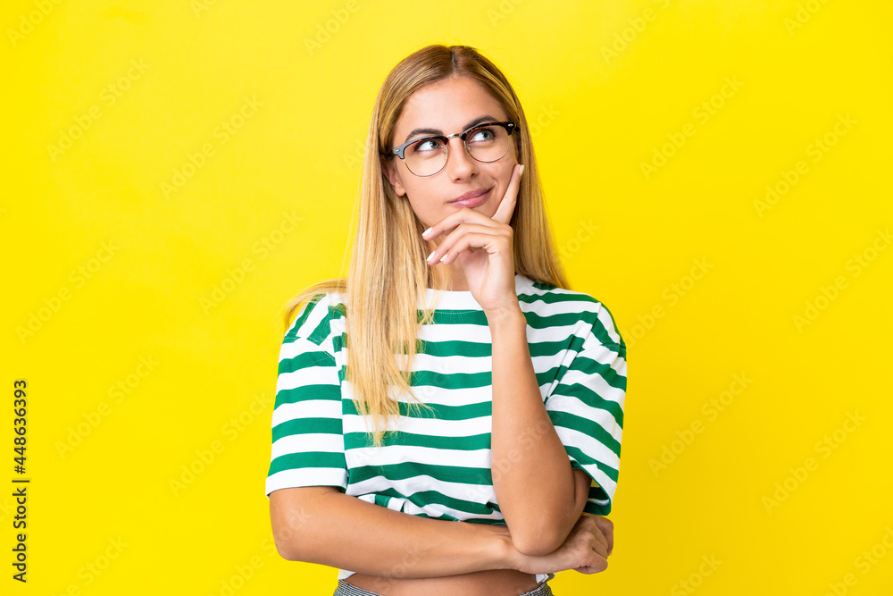 Blonde Uruguayan girl isolated on yellow background having doubts and thinking Blonde Uruguayan girl isolated on yellow background having doubts and thinking