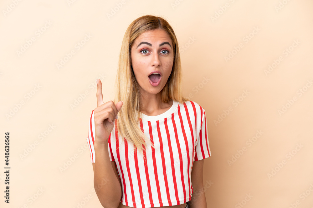 Blonde Uruguayan girl isolated on beige background intending to realizes the solution while lifting a finger up Blonde Uruguayan girl isolated on beige background intending to realizes the solution while lifting a finger up