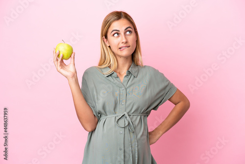 Young Uruguayan woman isolated on blue background pregnant and frustrated while holding an apple