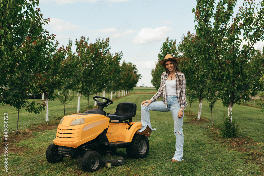 woman standing beside lawn mower in orchard woman standing beside lawn mower in orchard