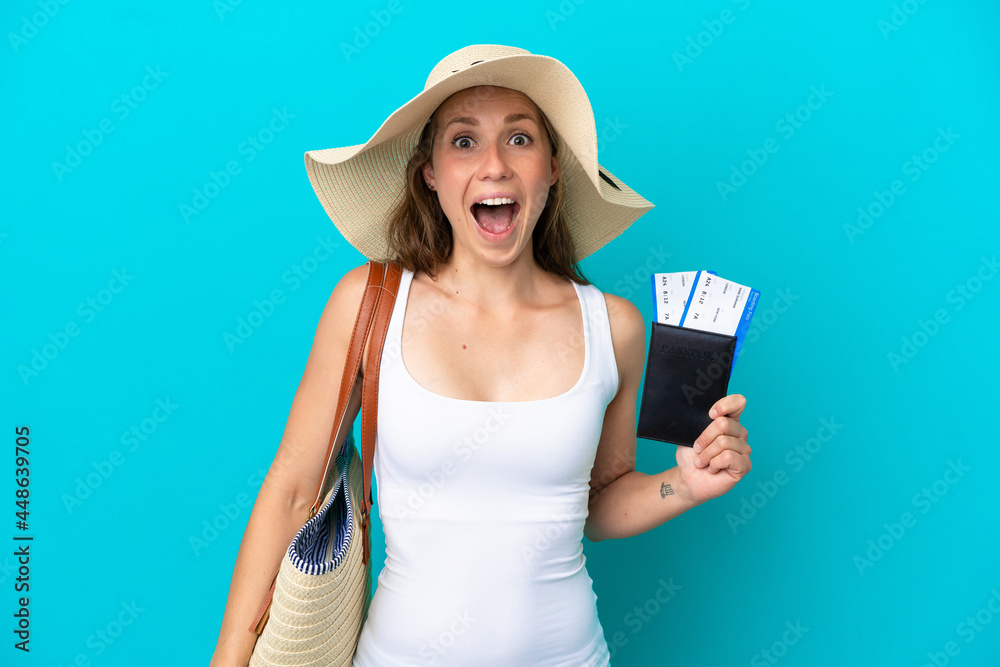 Young caucasian woman holding a beach bag and passport with pamel isolated on blue background with surprise and shocked facial expression Young caucasian woman holding a beach bag and passport with pamel isolated on blue background with surprise and shocked facial expression