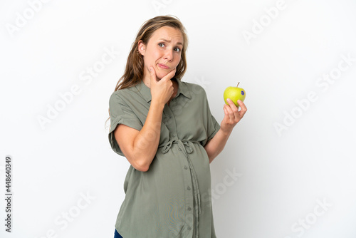 Young caucasian woman isolated on white background pregnant and holding an apple while thinking