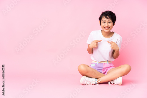 Young Vietnamese woman with short hair sitting on the floor over isolated pink background with surprise facial expression © luismolinero