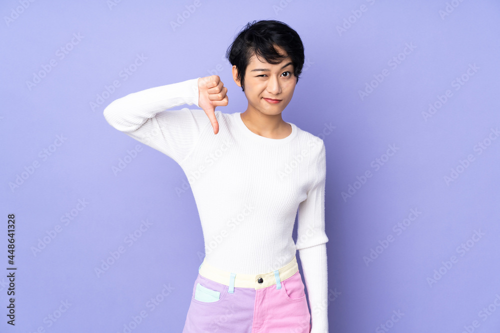 Young Vietnamese woman with short hair over isolated purple background showing thumb down with negative expression Young Vietnamese woman with short hair over isolated purple background showing thumb down with negative expression