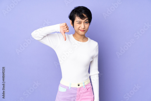 Young Vietnamese woman with short hair over isolated purple background showing thumb down with negative expression
