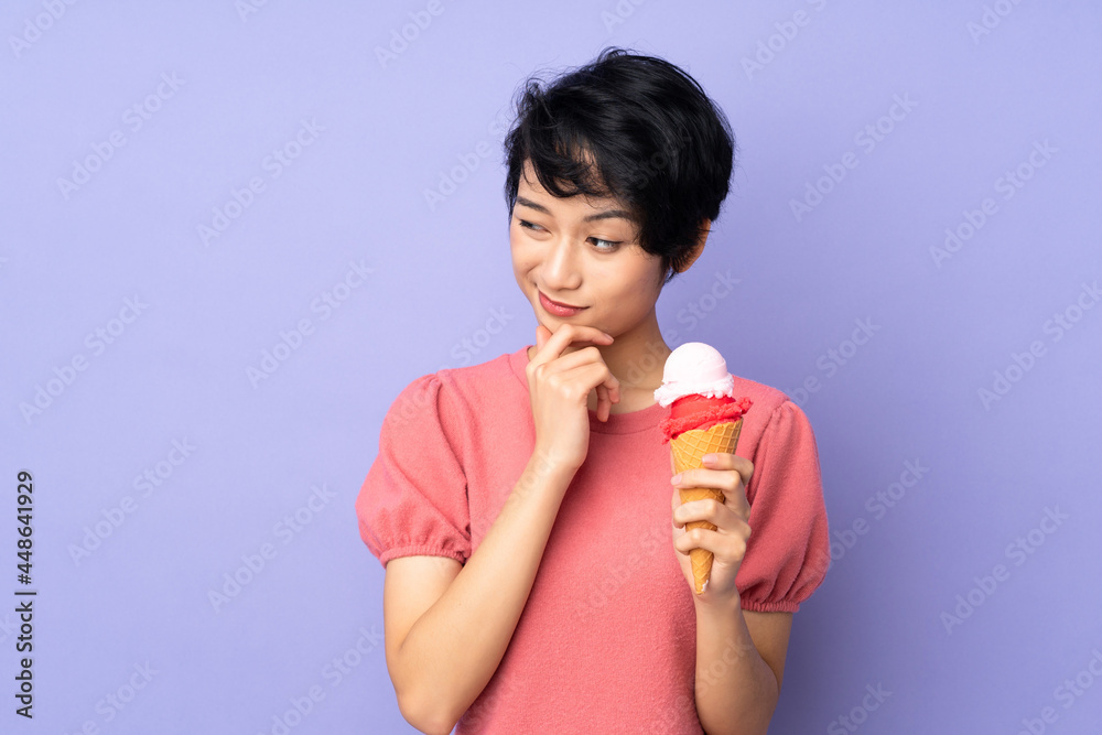 Young Vietnamese woman with short hair holding a cornet ice cream over isolated purple background thinking an idea and looking side Young Vietnamese woman with short hair holding a cornet ice cream over isolated purple background thinking an idea and looking side
